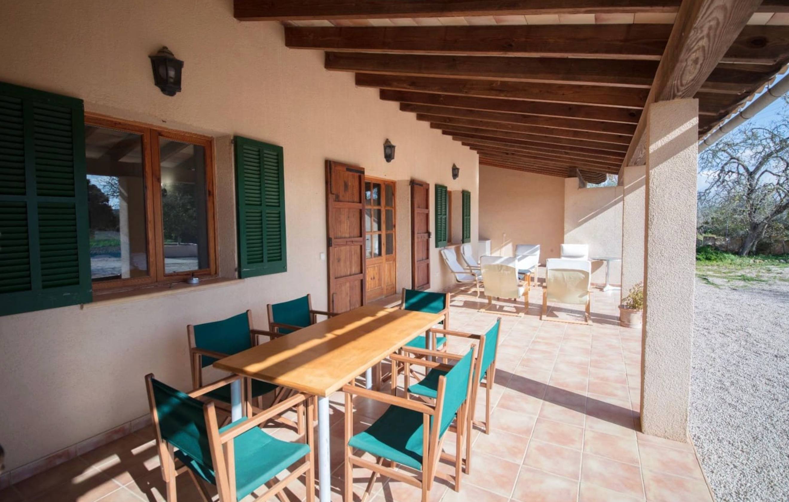 Covered terrace with wooden dining table and green shutters