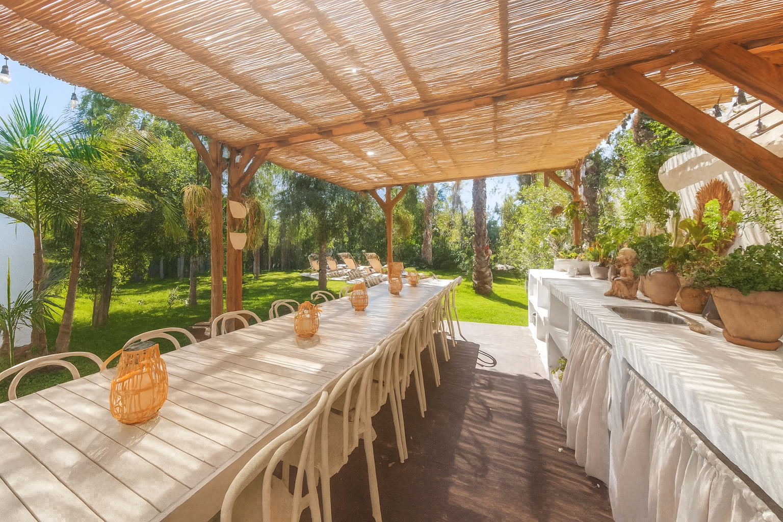 Outdoor dining area under wooden pergola with long table and buffet setup